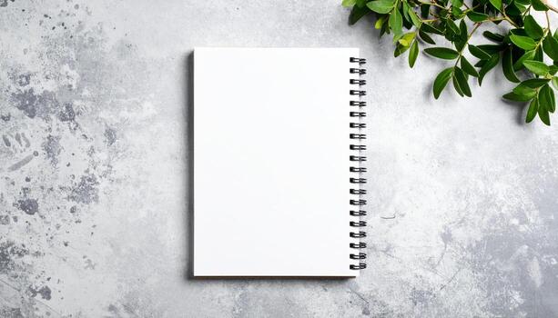 Pristine white spiral bound notebook rests on textured gray backdrop, inviting creativity with its blank pages. surrounding greenery adds touch of freshness and inspiration photo