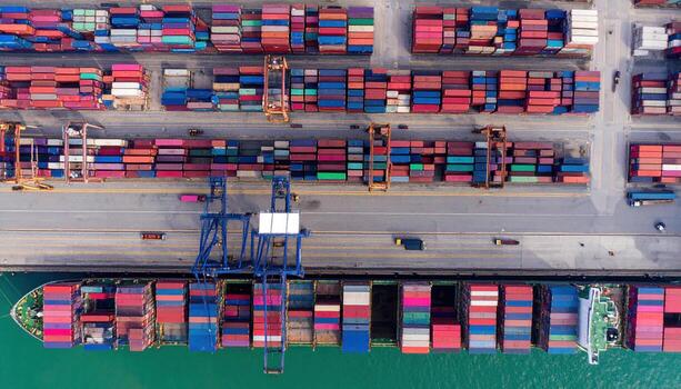 Aerial view of busy shipping port with colorful containers stacked along dock and cargo ship docked, showcasing industrial activity and maritime logistics photo