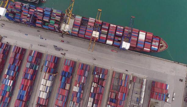 Aerial view of busy shipping port with cargo containers and cranes, showing large cargo ship docked at port, surrounded by water and infrastructure, conveying transportation and logistics activity photo