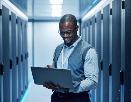Man in data center smiles while using laptop, surrounded by server racks and illuminated by blue lights photo