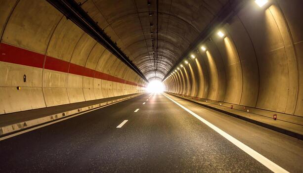 Long tunnel with bright light at end, illuminated by overhead lights, showing smooth asphalt road with lane markings and safety barriers, creating sense of journey and transition photo