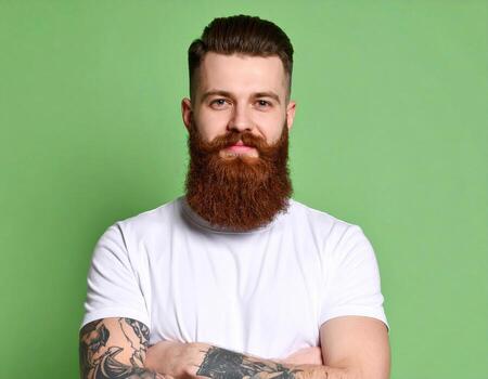 A man with a beard and tattoos standing in front of a green background photo