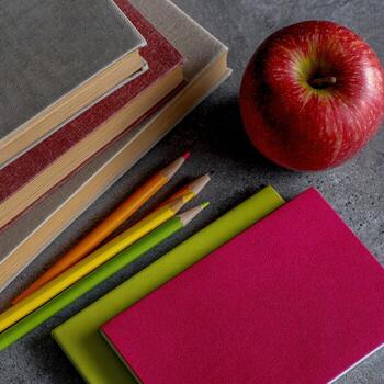 A stack of books, an apple, and pencils photo