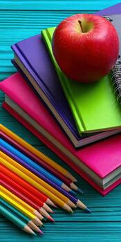 Colorful pencils and an apple on a blue table photo