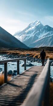A man walking across a bridge over a river with mountains in the background photo