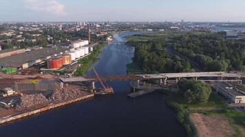 antenn se av riga, lettland, som visar en flod kantad förbi grönska och industriell faciliteter, med en bro och stadsbild synlig i dagsljus. video