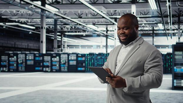 System administrator in data center workplace uses tablet to calibrate energy usage. Server farm IT expert using device to inspect UPS configurations, doing maintenance on equipment, camera A photo