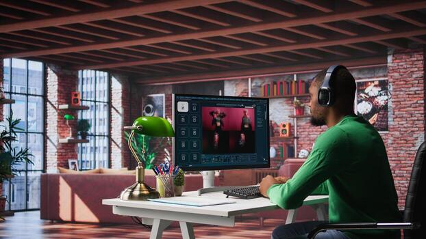 African American worker using program with photos in a modern loft. Young man creating visual content with deep learning models and prompts on monitor with AI interface. Camera B.