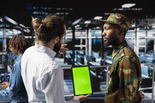 Army tech soldier and engineers using green screen on tablet, troubleshooting computer systems for a national defense military mission. Officer and server farm admins on industrial platform. photo