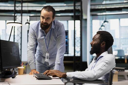 Manager supervising technician in wheelchair using AI on computer to optimize performance and forecast issues. Team leader and employee with disability in inclusive office train deep learning models photo