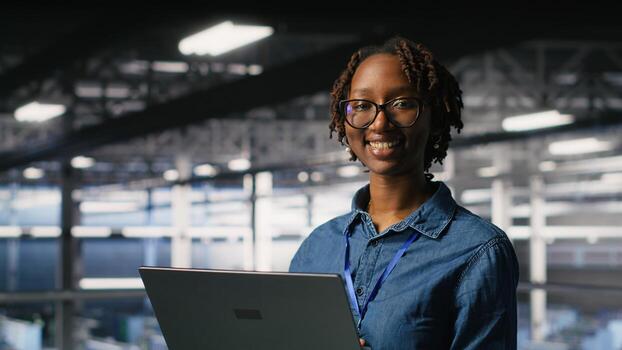 Happy woman in data center doing maintenance tasks on laptop, ensuring optimal performance. Engineering team reviewing diagnostics and applying patches to server room, improving stability photo