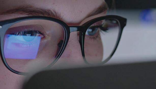 Close up of eyes behind eyeglasses reflecting a laptop screen with copy space background, suitable for technology themes, digital lifestyle concepts, remote work, internet browsing, online learning, photo