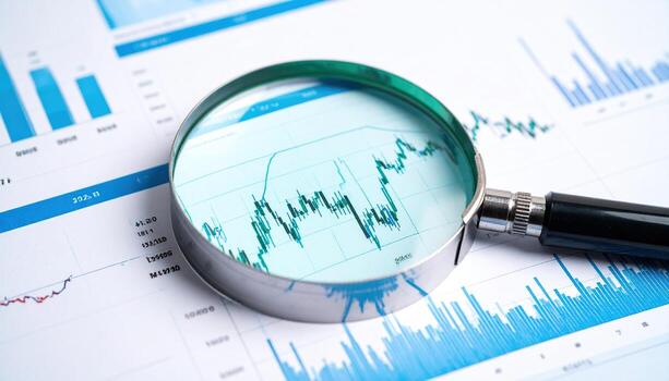 Close up photo of printed financial chart with magnifying glass, highlighting analysis, investment, stock market, data review, corporate finance, and economic business concept.