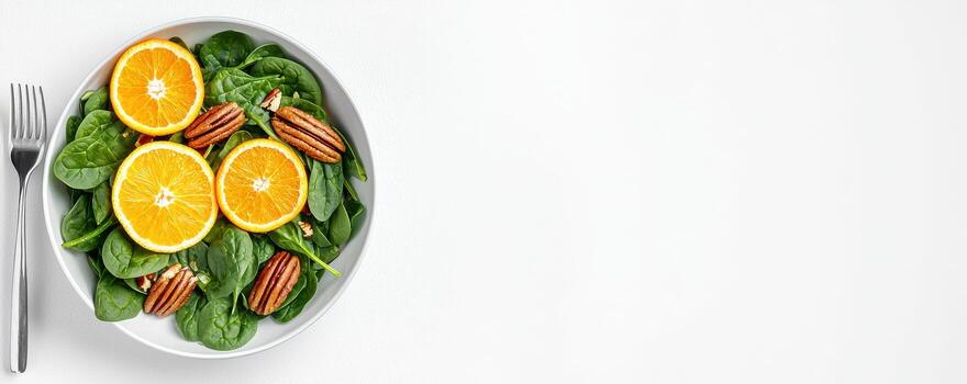 Spinach salad with orange slices and toasted pecan nuts on white plate with fork photo