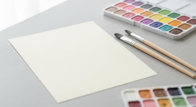 Blank paper with watercolor paint palette and brushes on a light gray table, ready for art creation photo