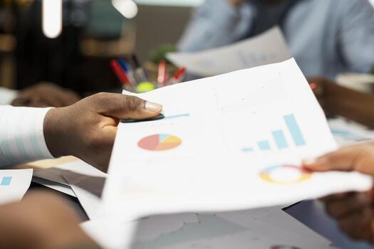 Close up of diverse business staff exchanging reports files and insights to forecast company objectives in a quiet strategy room after hours at night. Workers collaborating on finance projections. photo