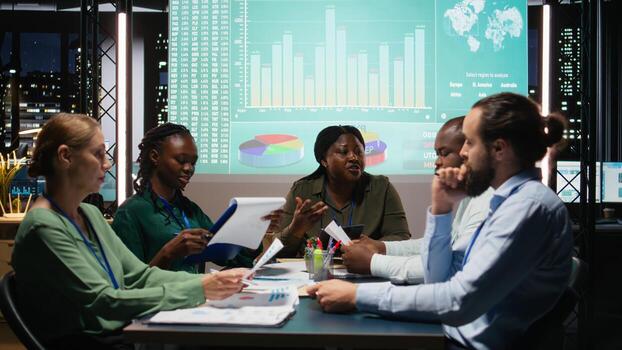 Multiethnic group of advisors reviewing data insights and financial situation on papers, preparing updates for the shareholders and establishing the project agenda and objectives. Camera A. photo