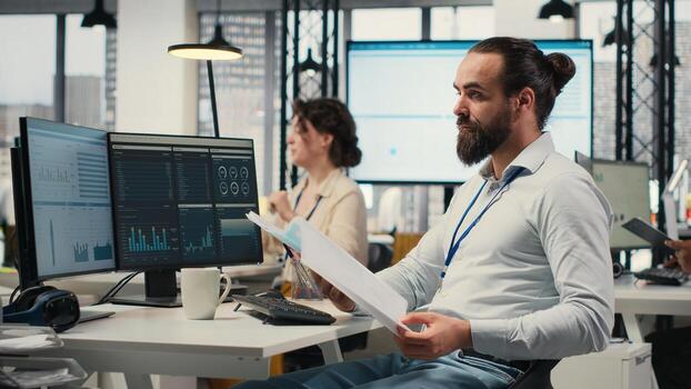 Office employee reviewing KPI metrics on monitor and analytics on files, building a vision and business strategy to accomplish objectives and success. Maintaining a professional mindset. photo