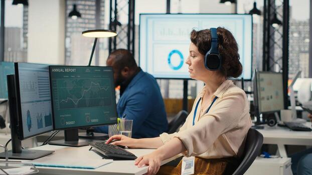 Office administrator uses focus music on headset to solve tasks, monitoring performance metrics at the workstation. Administrative tasks to ensure enterprise productivity and success. Camera B. photo