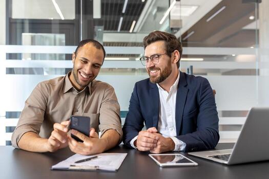 Two business professionals smiling while discussing work using a smartphone and tablet at their workplace. The modern office environment emphasizes teamwork, collaboration, and technology. photo