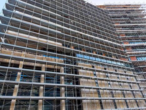 Facade of tall building covered in scaffolding. Symbol of engineering, progress and structural development in urban space photo