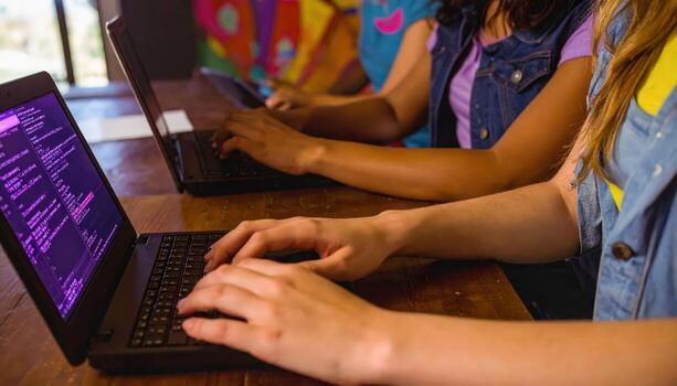 Three people are typing on laptops at a table. One of the laptops has a purple screen. Scene is focused and serious, as the people are working on their laptops photo
