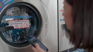 une moderne individuel est absorbé dans le blanchisserie expérience en utilisant une intelligent dispositif à naviguer le soi un service machinerie. video