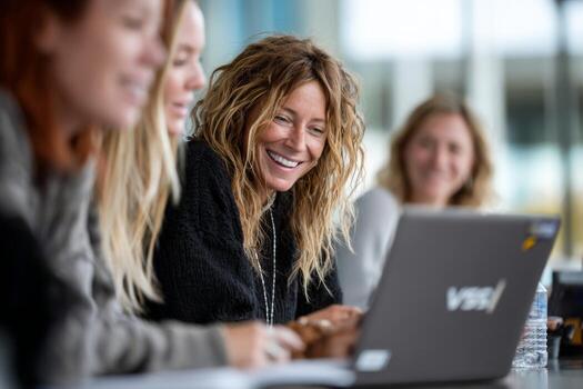 Three women smiling while sitting at a table with a laptop photo