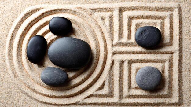 Black and grey stones resting on a serene sand surface with circular and rectangular patterns photo