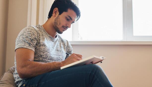 Man Seated by Window, Engaged in Writing Within a Notebook photo