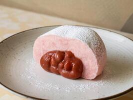 A soft pastel pink dessert filled with a rosy red filling, dusted with powdered sugar. photo