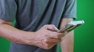 närbild en man använder sig av smartphone i främre av grön skärm, som visar modern mobil användande, representerar digital kommunikation, teknologi, och modern anslutning video