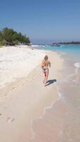 antenn se av en kvinna löpning längs de sandig tropisk strand med turkos hav på gili öar, Indonesien. exotisk sommar livsstil, aktiva Semester, frihet, och äventyr resa i Asien. video