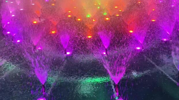 A dynamic water fountain is illuminated with colorful lights, creating a mesmerizing visual experience for all photo