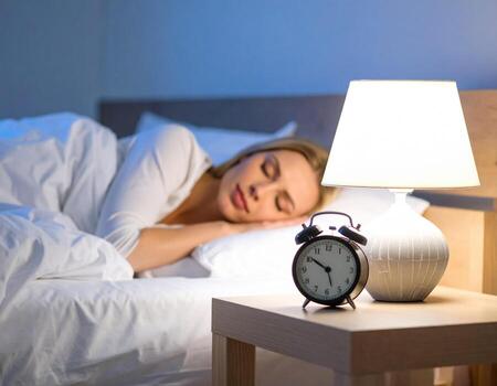 Woman sleeps peacefully in cozy bedroom, surrounded by soft bedding and warm lamp illuminating space. clock on bedside table shows late hour, enhancing serene atmosphere photo