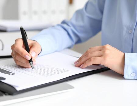 Person writing on document with pen at desk, showcasing focus and productivity in office environment photo