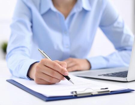 Person writing on document with pen while sitting at desk with laptop nearby, showcasing focus and productivity photo