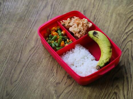 A red container with rice, vegetables, and a banana photo