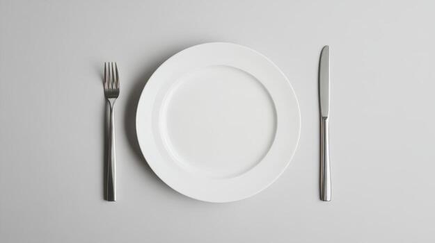 Empty white plate surrounded by fork and knife on a minimalist gray background ready for dining or food presentation photo