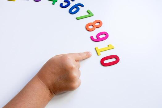 Child pointing at number sequence with colorful wooden numbers on white surface photo