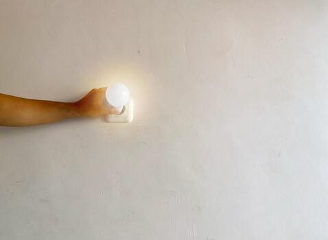 Hand installing a light bulb into a wall socket providing bright illumination indoors. photo
