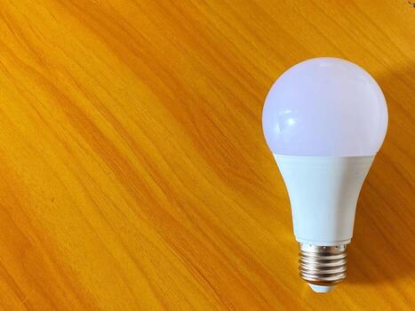 Energy efficient light bulb rests on a textured golden casting a soft glow. photo