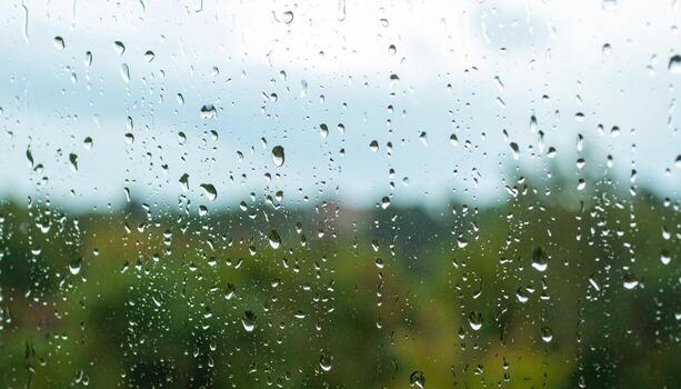 Raindrop water droplets on glass window with blurred green landscape background creating calm and peaceful rainy day atmosphere photo