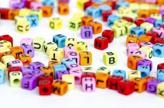 A wide spread of small colorful transparent cubes with printed letters forming a random mix scattered across a bright background symbolizing creativity and learning photo