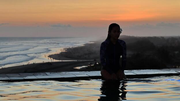Calm. pose. Silhouette of Woman in Infinity Pool Watching Ocean Sunset with Crowded Beach and Colorful Sky photo