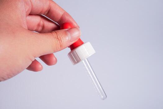 Hand holding pipette with red lid isolated on horizontal copy spaced plain background. photo