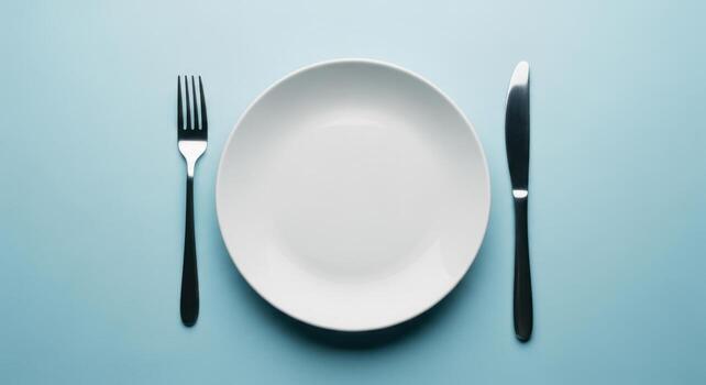 Empty white ceramic plate with fork and knife on a minimalist light blue background photo