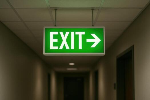 Bright green illuminated EXIT sign with right arrow hanging in a dimly lit hallway photo