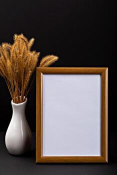 Halloween. Mockup. Empty wooden frame stands against dark backdrop, near vase of dried grass, creating perfect setting for Halloween decoration inspiration and creative design possibilities. Vertical photo