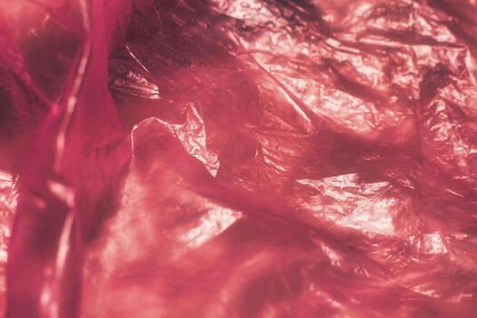 Close-up of crumpled pink plastic wrap with a shiny, reflective surface. Perfect for abstract, modern, or vibrant backgrounds with a textured, glossy finish. photo